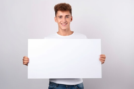Happy young man holding blank white banner sign, isolated studio portrait.