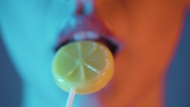 Extreme close-up red lips licking a yellow lemon lollipop, blue orange lightning