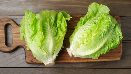 Iceberg lettuce on cutting board on wooden table background, top view. Two whole heads of fresh...