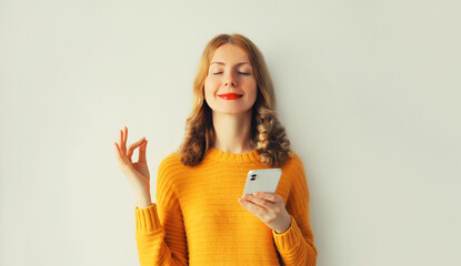 Young smiling happy woman with phone having luck keeps calm or meditates with closed her eyes on...