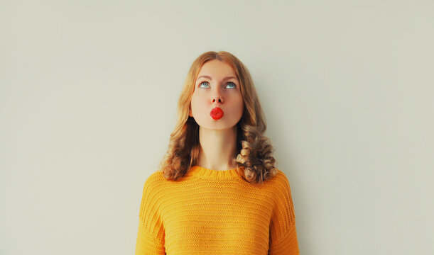 Portrait of beautiful wondering young woman thinks looks up, female caucasian 20s model blowing her lips with red lipstick wearing yellow sweater on white background