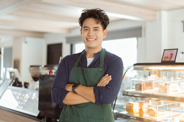Young Asian male barista in apron having arms folded and smiling while looking at camera with copy space - 629408362