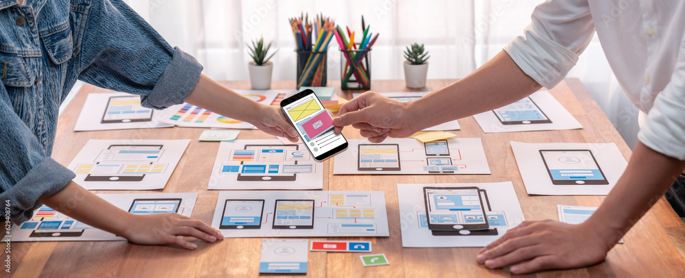 Poster Panorama shot of front-end developer team brainstorming UI and UX designs for mobile app on paper wireframe interface. User interface development team planning for user-friendly UI design. Scrutinize