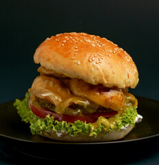 Close-up of a delicious fresh homemade burger with lettuce, cheese, onion and tomato on a rustic wooden board on a dark background