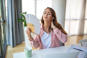 A young woman sweats profusely while working on her laptop in an overheated home office. With no...