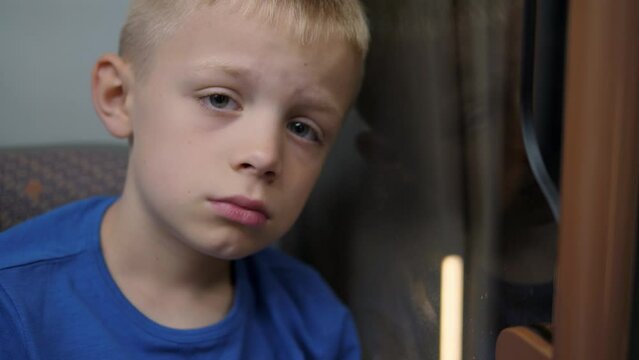 A close-up portrait of a sad little boy in a subway car, he leans on the glass and looks sadly into the camera. The child got lost in the subway.