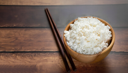 hot cooked rice in wooden bowl and wooden chopsticks on wooden floor dark background.