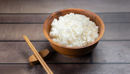 hot cooked rice in wooden bowl and wooden chopsticks on wooden floor dark background.