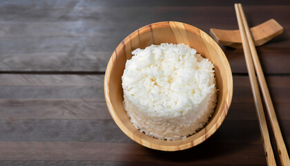 hot cooked rice in wooden bowl and wooden chopsticks on wooden floor dark background.