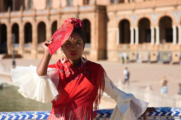 Young black woman dressed as a flamenco gypsy in a famous square in Seville, Spain. She wears a...