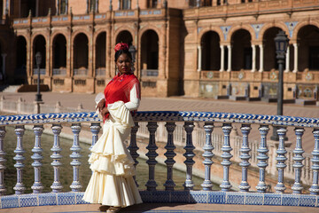 Young black woman dressed as a flamenco gypsy in a square in Seville, Spain. She wears a beige...
