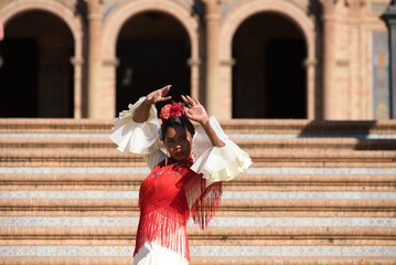 Young black woman dancing flamenco in a square in Seville, Spain. She wears a beige dress with...