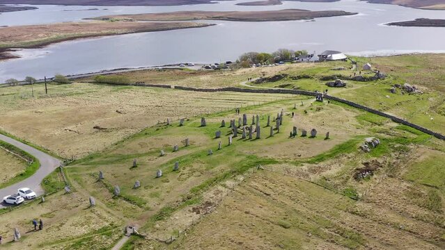 Tilting drone shot of the Callanish Standing Stones on the Isle of Lewis, part of the Outer Hebrides of Scotland. Filmed on a sunny, summers day. Tourists and visitors are visible.
