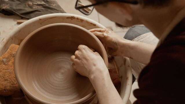 Potter making ceramic plate or plate on pottery wheel. Two hands create bowl. Top view. Potter shapes clay product. Close-up in 4K, UHD