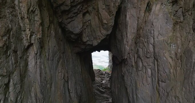 Drone reveal pink jacket woman by hole through Torghatten mountain entrance