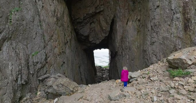 Drone fly over woman in pink jacket toward huge hole through Torghatten mountain