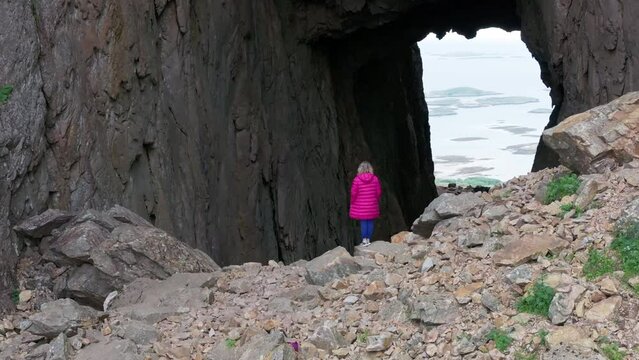 Woman in pink jacket by hole through Torghatten mountain entrance; drone reveal