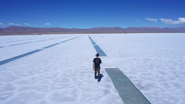 Young man walks by extracted rows of salt at salt flats in Argentina