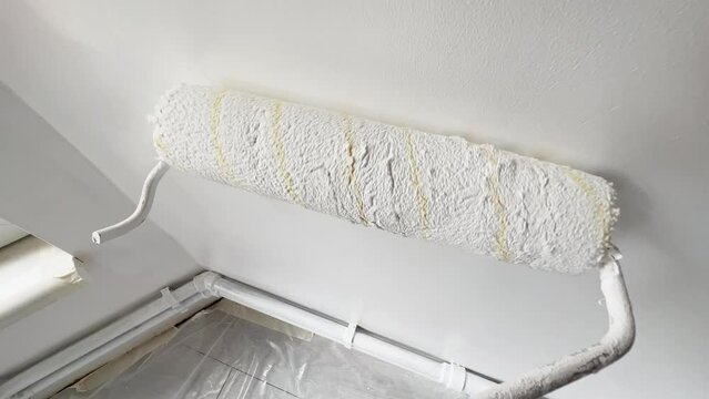 Painting the wall with a paint roller in white.