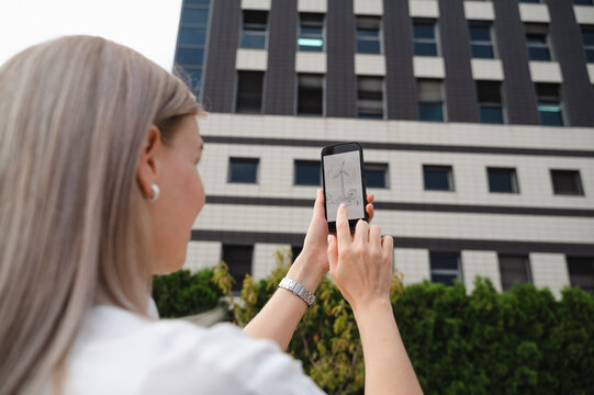Businesswoman examining wind turbine drawing on smart phone in front of building