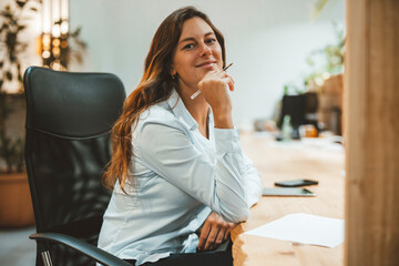 Smiling businesswoman sitting with hand on chin at desk