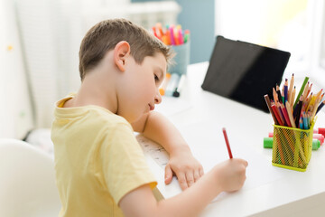 Smiling boy drawing with colored pencil near tablet pc at home