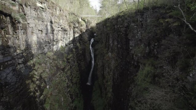 Drone shot flying away from big waterfall inside narrow and rocky Corrieshalloch gorge in Scottish Highlands