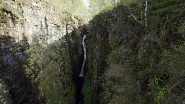 Drone shot flying towards a big waterfall inside narrow and rocky Corrieshalloch gorge in Scottish Highlands