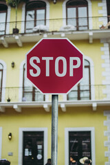 Stop red sign in front of a yellow building with windows. Blurred background. Road sign of obligation, stop and give priority to other cars in the street.