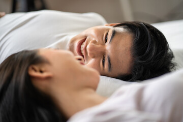 Asian new marriage couple lying down on bed and looking at each other. 