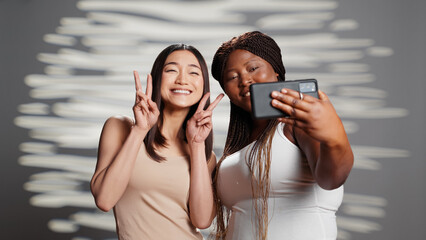 Happy flawless girls taking photos on mobile phone, using smartphone to have fun with pictures. Curvy and skinny ladies promoting self love and body acceptance, self confidence on camera.