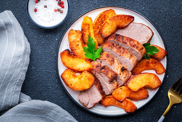 Baked pork tenderloin with sweet quince or apple slices served on white plate. Black table background, top view