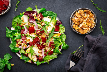 Gourmet salad with beetroot, pear, arugula, lettuce, red onion, chard and walnut, black kitchen table. Fresh delicious dish for healthy eating
