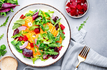 Beetroot, feta cheese and tangerine healthy salad with arugula, lettuce, red onion on gray kitchen table. Fresh useful dish for healthy eating