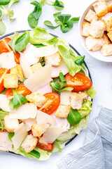 Classic Caesar salad with chicken, iceberg salad, croutons, parmesan cheese and caesar dressing. Black table background, top view