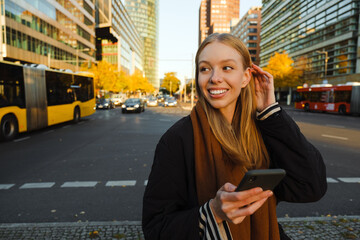Smiling woman using smartphone while standing at busy street