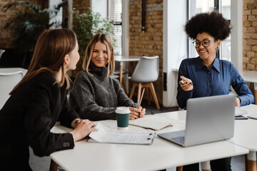 Three smiling women having conversation while working in office