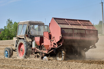 Spring sowing on farmer field, an agricultural wheeled tractor with hitched potato planter rides on arable land.