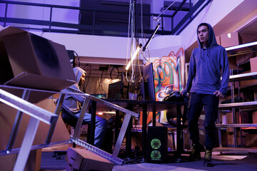 Hacker leaving abandoned warehouse after hacking network system. Asian criminal standing in hideout place after doing crime activity and breaking into online server at night
