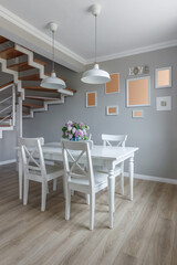 Large dining table in a modern house, with white chairs and a beautiful bouquet of lilacs in a blue vase