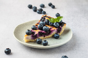 A piece of shortbread pie with blueberries with a mint leaf in a plate on a gray background, horizontal.