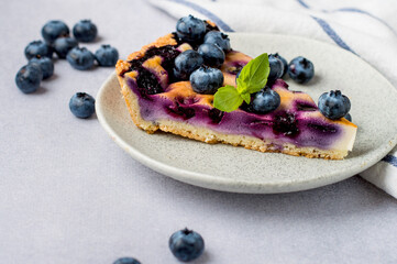 A piece of blueberry shortbread pie with a mint leaf in a plate, on a gray background, horizontal.