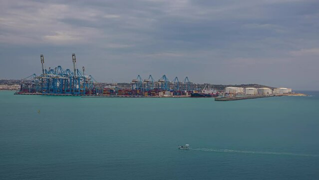 Timelapse shot of large blue crane loading over a large container ship in Kalafrana, Birzebbuga, Malta on a cloudy day. 