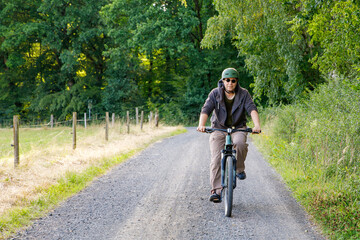 Fototapeta premium Mountain biker riding on bike in summer forest landscape. Active middle-aged man cycling on bicycle, sports and leisure activity.