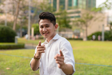 An assured young asian man makes a double finger gun gesture. Outdoor city scene.