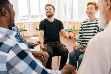 Group of happy multiracial people holding hands sitting in circle during therapy session. Cheerful...
