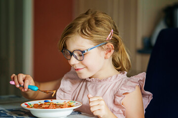 Little preschool girl eating from spoon vegetable potato soup. Healthy food for children. Happy kid at home or nursery.