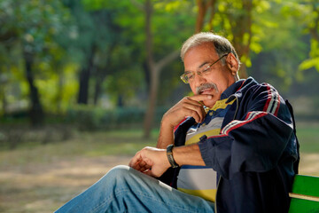 Indian man sitting at park and looking time in wristwatch.