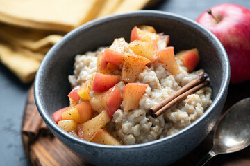 Gluten free oatmeal porridge with apple and cinnamon in a bowl, closeup view. Autumn comfort food - obrazy, fototapety, plakaty