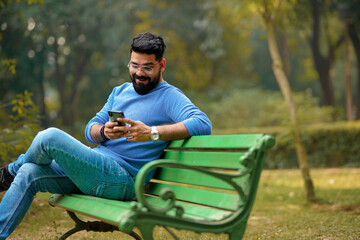 young indian man using smartphone at park.